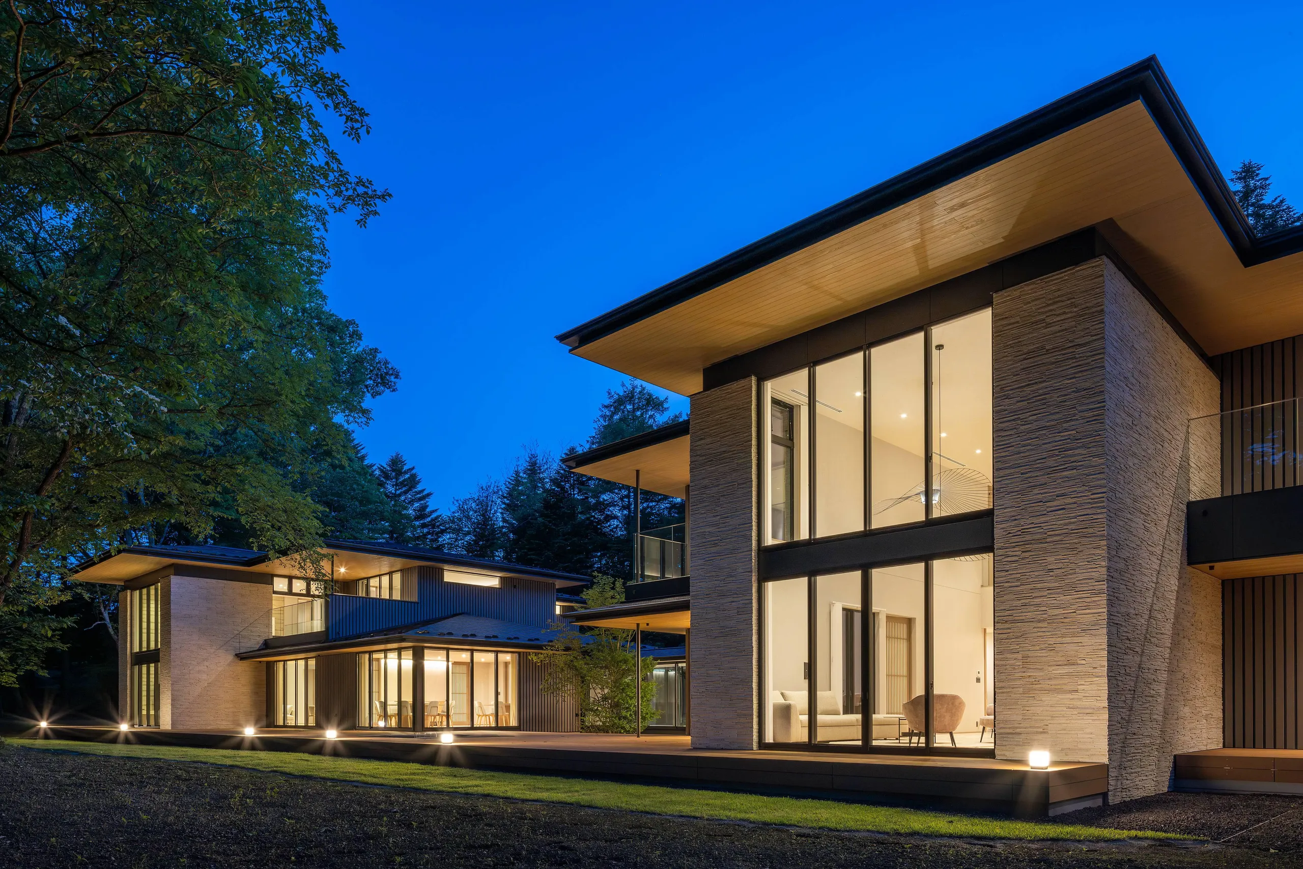 Exterior view of the Karuizawa estate at dusk, showcasing the main residence and guest house surrounded by forest.